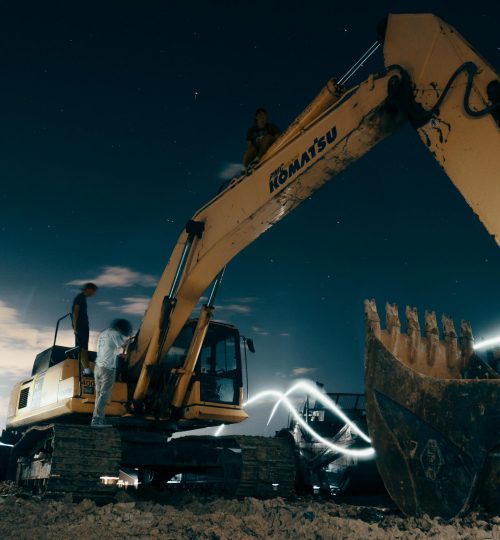 A powerful excavator at a construction site under the night sky, with workers around.